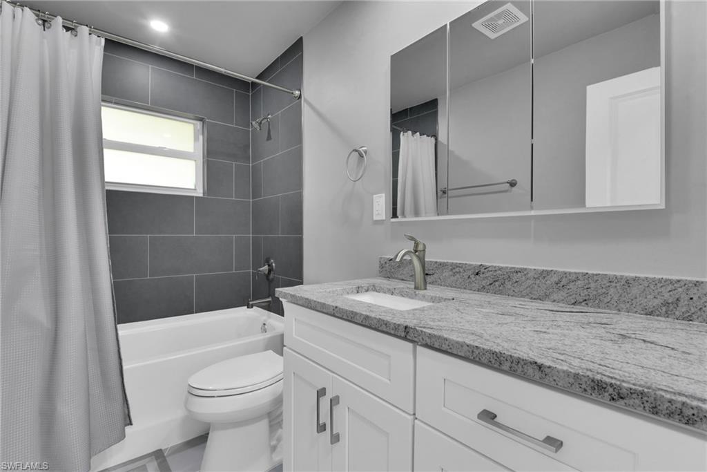 Bathtub with grey subway tile surround, white vanity with granite-finish countertop, undermount sink, and multi-panel mirrored medicine cabinet