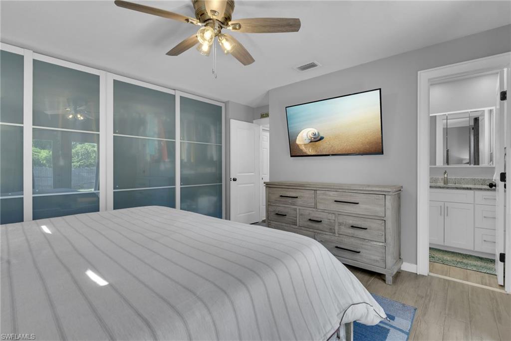 Integrated frosted glass wardrobe system, ceiling fan with light fixture, wood-finish flooring, white paneled door, and adjacent bathroom with white vanity