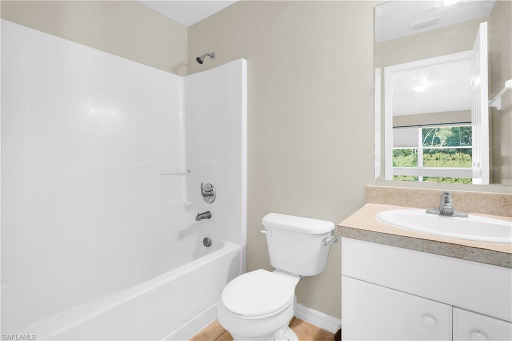 White bathtub with integrated shower, chrome fixtures, single vanity with integrated sink, and a framed mirror