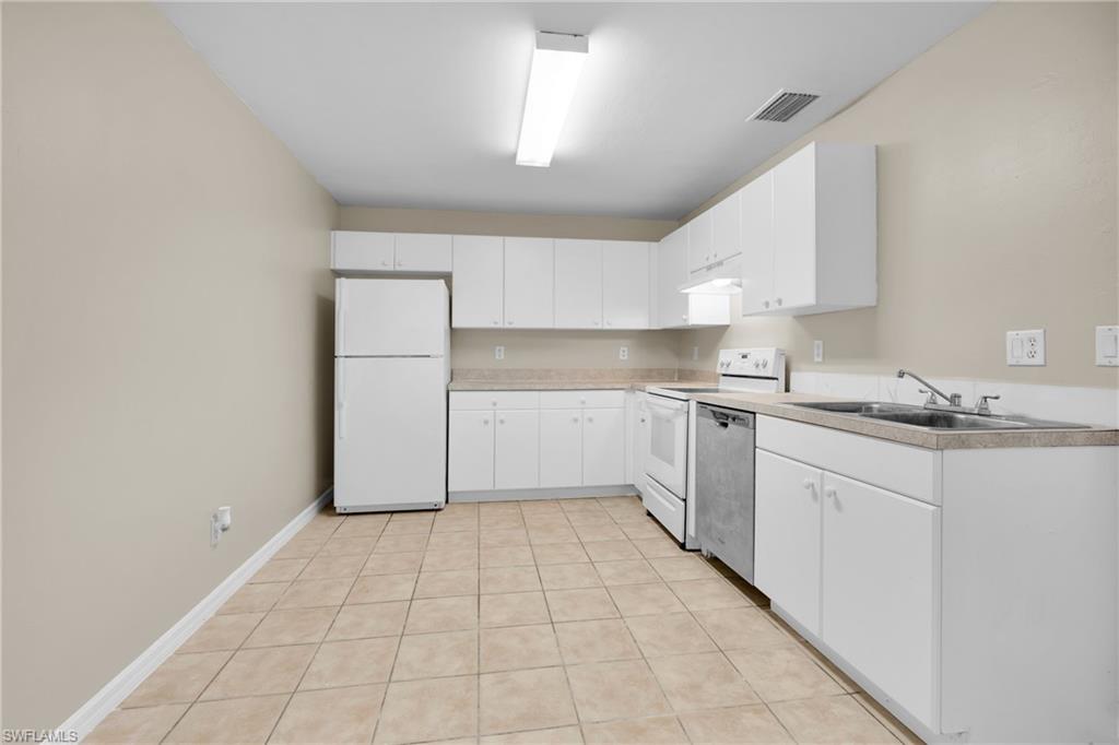 Kitchen featuring white cabinetry, light-toned countertops, tile flooring, and white appliances