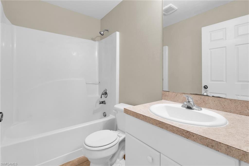 Bathroom featuring a white integrated tub and shower unit, a vanity with an integrated sink, and a light-colored countertop