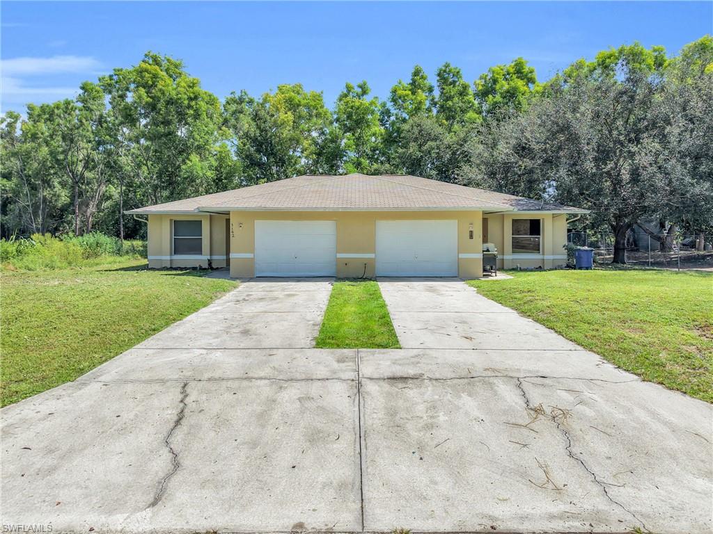 Duplex exterior with attached garage doors, concrete driveway, and front lawn