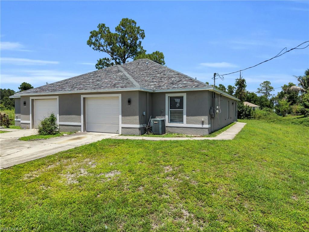 Stucco exterior with a shingled roof, featuring two garage doors, a concrete walkway, and an air conditioning unit