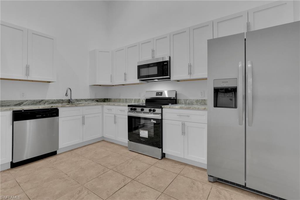 White cabinetry with brushed nickel hardware, stainless steel appliances, speckled countertops, and tiled flooring