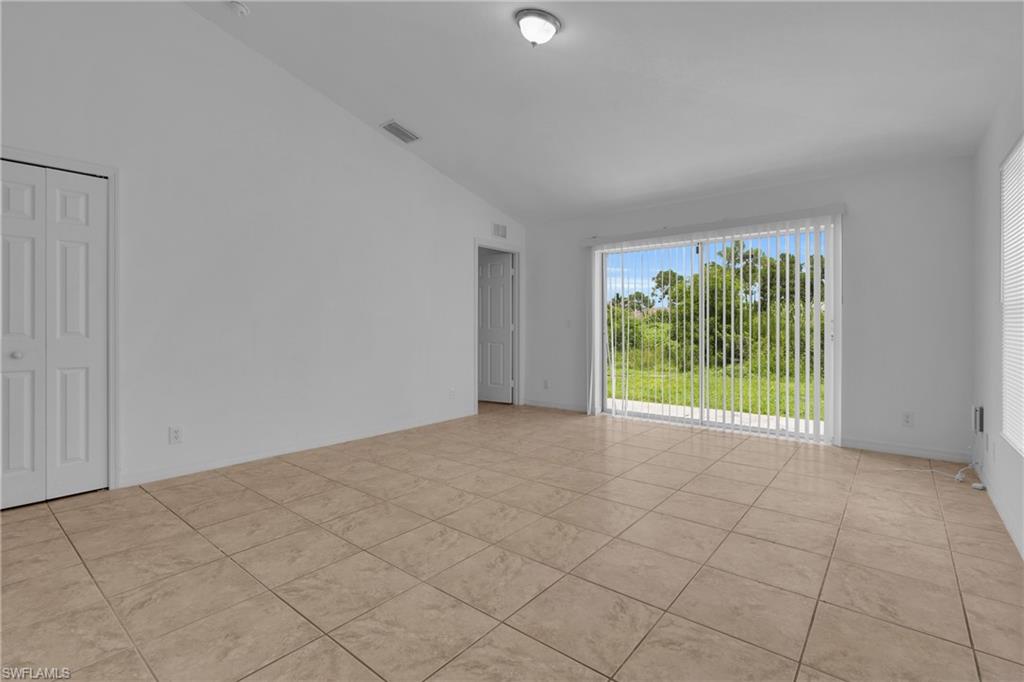 Neutral-toned tile flooring, vaulted ceiling, and sliding glass doors with vertical blinds