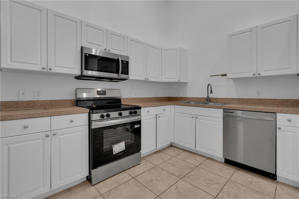 Kitchen featuring white cabinetry, stainless steel appliances, light brown countertops, and tiled flooring