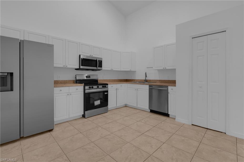 Kitchen featuring white cabinetry, stainless steel appliances, speckled countertops, and tile flooring