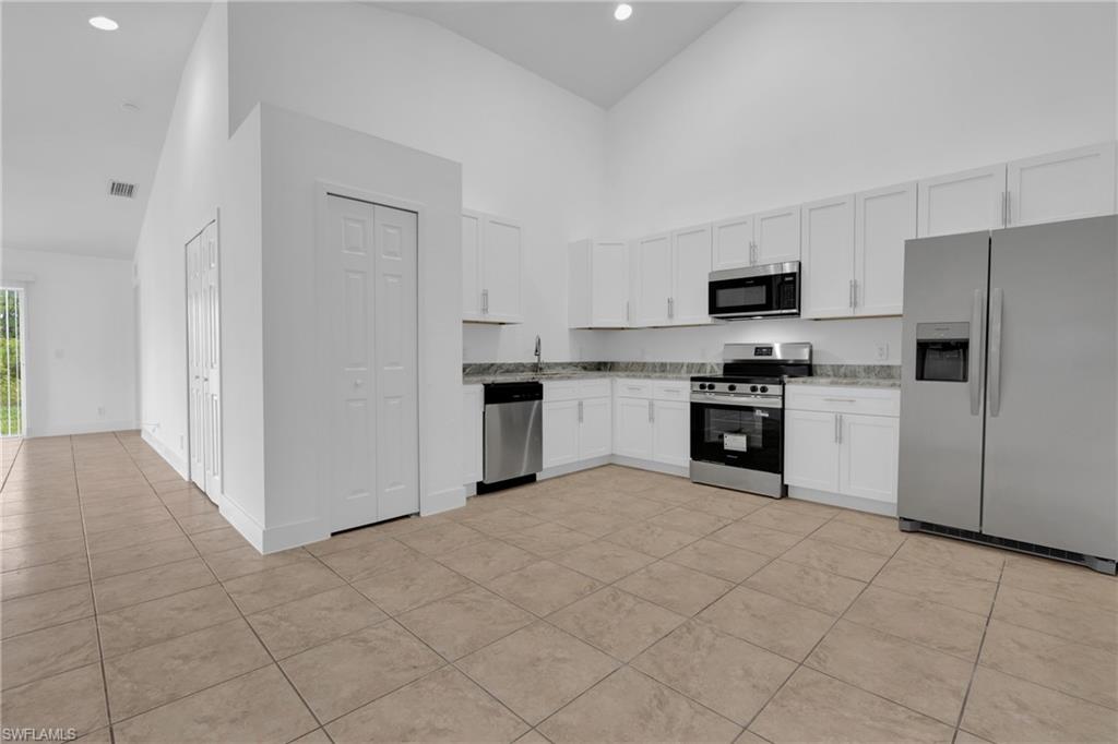 Kitchen featuring stainless steel appliances, white cabinetry, L-shaped countertop, and tile flooring