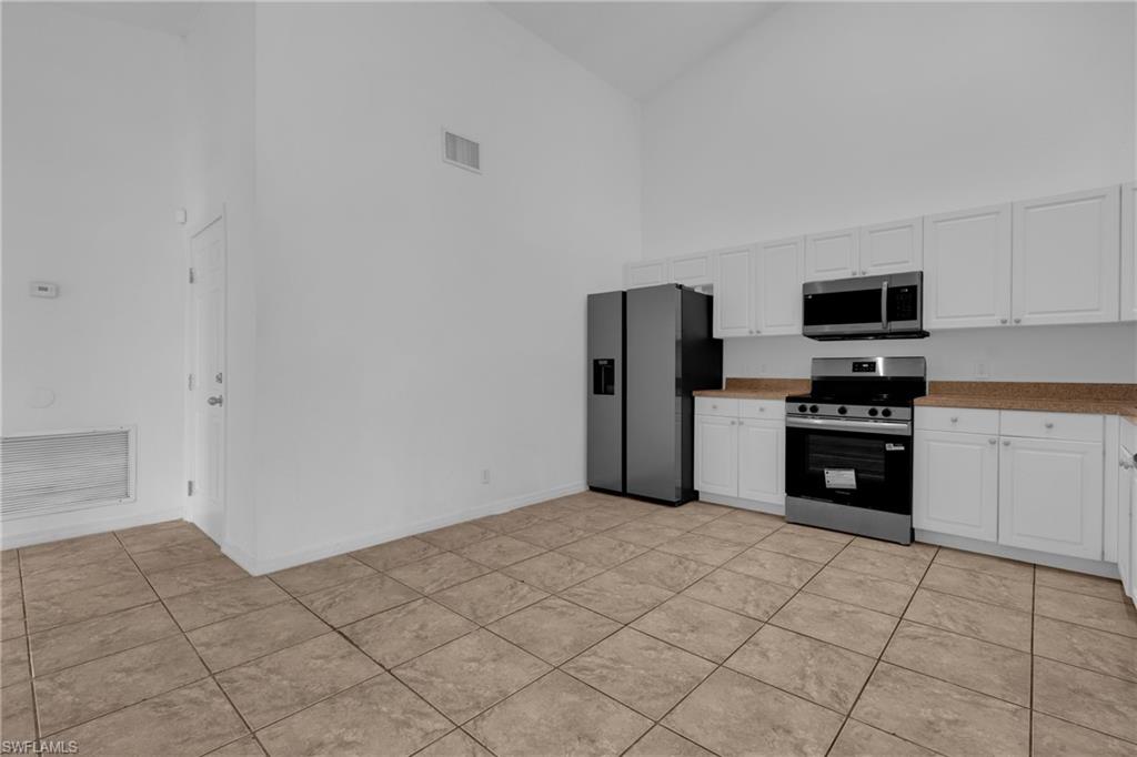 Vaulted ceiling, white cabinetry, stainless steel appliances, and tile flooring