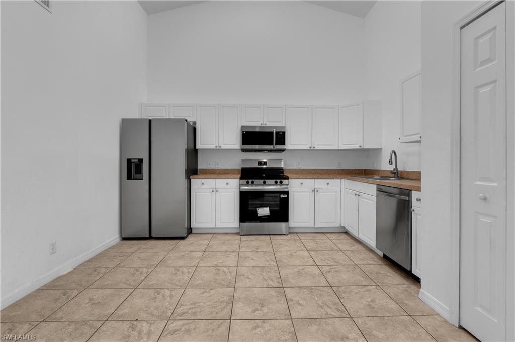 Kitchen featuring vaulted ceilings, white cabinetry, stainless steel appliances, and tile flooring