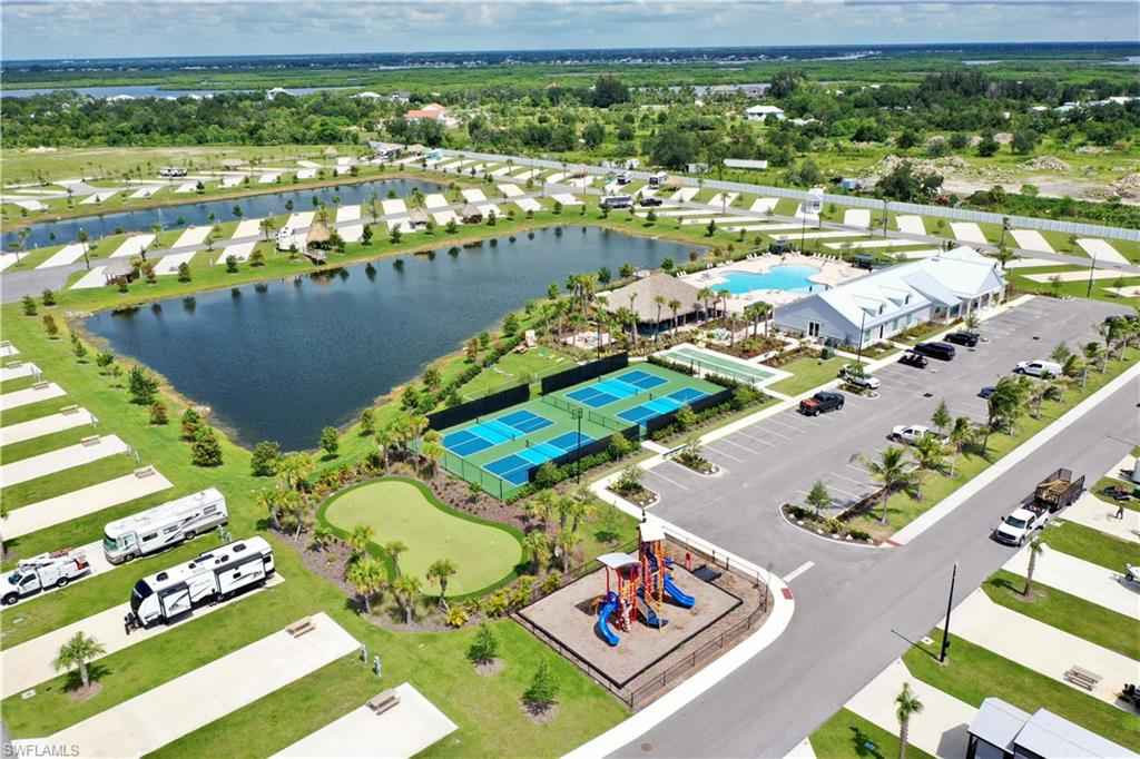 Expansive property featuring multiple RV lots, a large central pond, a community building with an outdoor pool, tennis courts, and a putting green