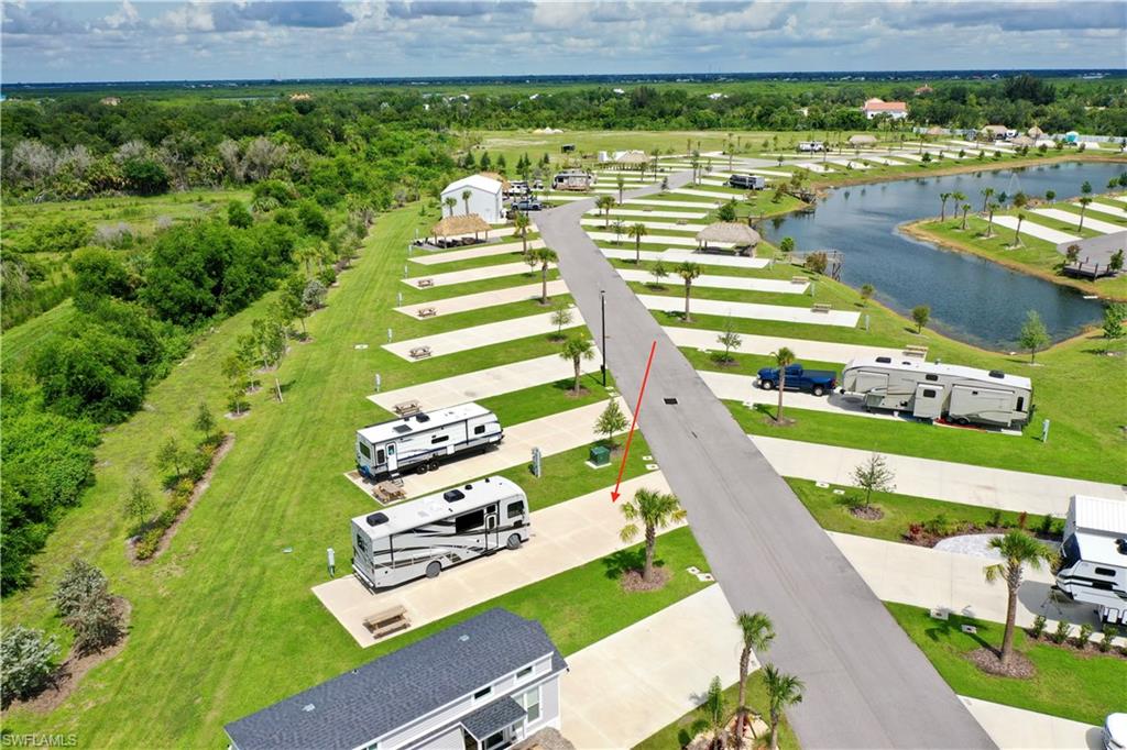 Paved road with dedicated parking pads, manicured green spaces, mature landscaping, and an adjacent water feature