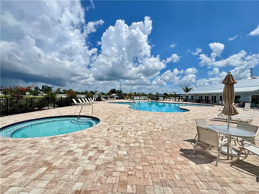 Expansive paver patio with a built-in spa, large swimming pool, and a community building