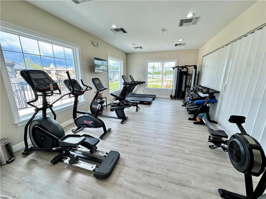 Fitness center featuring multiple exercise machines, wood-finish flooring, recessed lighting, and large windows with privacy blinds
