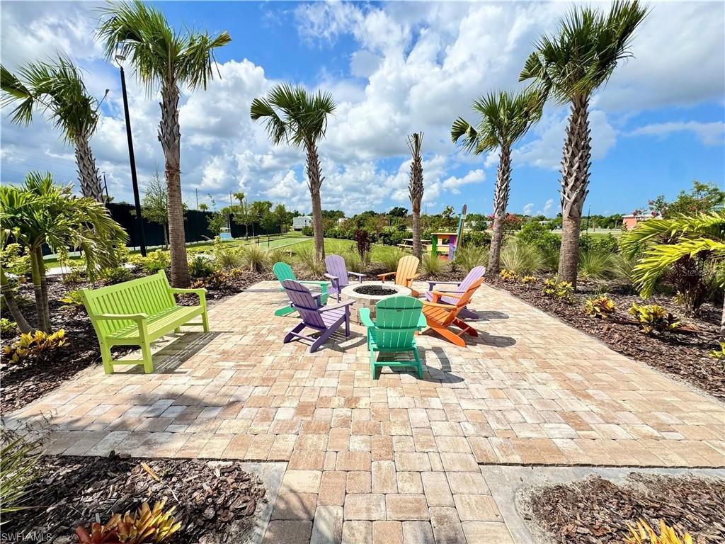 Paver patio featuring a built-in fire pit, surrounded by landscaped plantings and mature palm trees