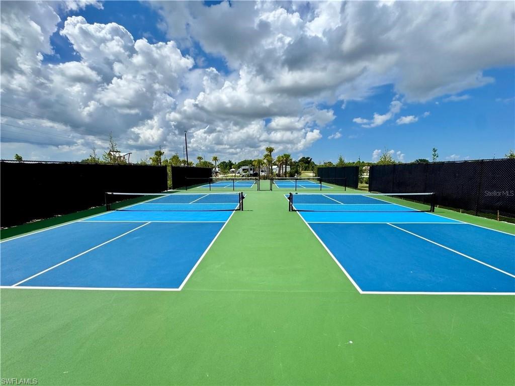 Multiple outdoor pickleball courts with vibrant blue and green surfacing, black privacy screening, and court lighting