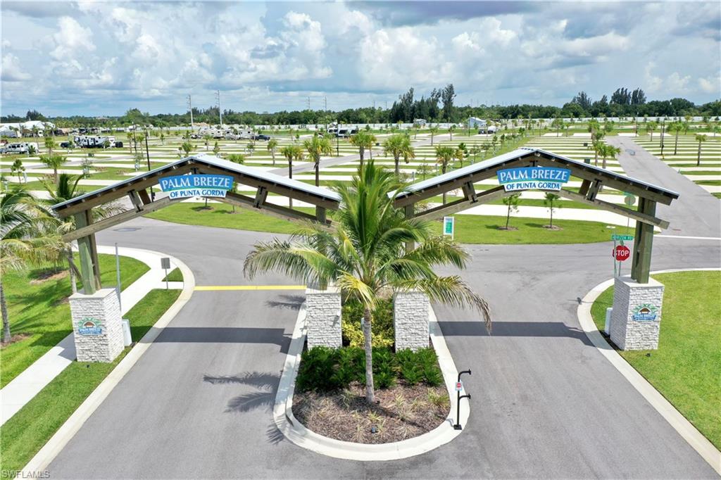 Entry archway with wood-look beams and stone-finish pillars, paved roads, and extensive level parking spaces