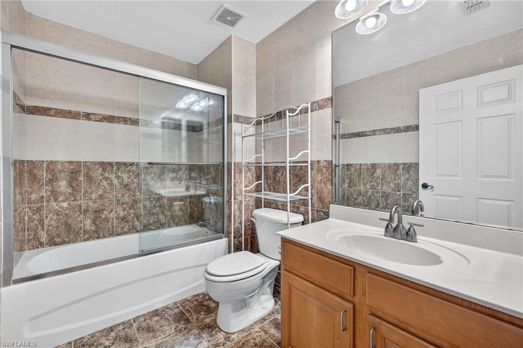 Bathtub with sliding glass enclosure, wood-finish vanity with integrated sink, full-width mirror, and tile flooring