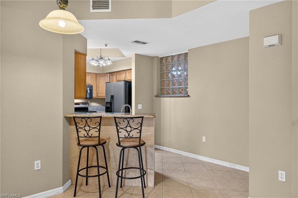 Breakfast bar with a stone-finish countertop, stainless steel kitchen appliances, wood cabinetry, and a glass block window feature