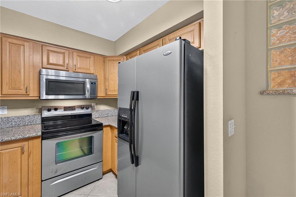 Kitchen featuring stainless steel appliances, wood cabinetry, stone countertops, and tiled flooring