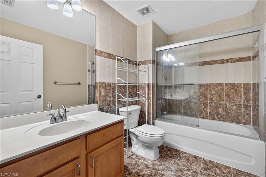 Bathroom featuring a wood-finish vanity with an integrated sink, a large wall mirror, and a full-size bathtub with a sliding glass enclosure