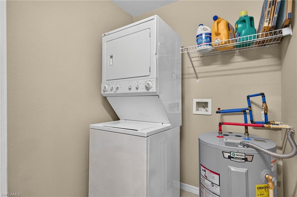 Dedicated laundry room featuring a stackable washer and dryer unit, stainless steel shelving with storage for cleaning supplies, wall-mounted thermostat, and neutral finishes throughout