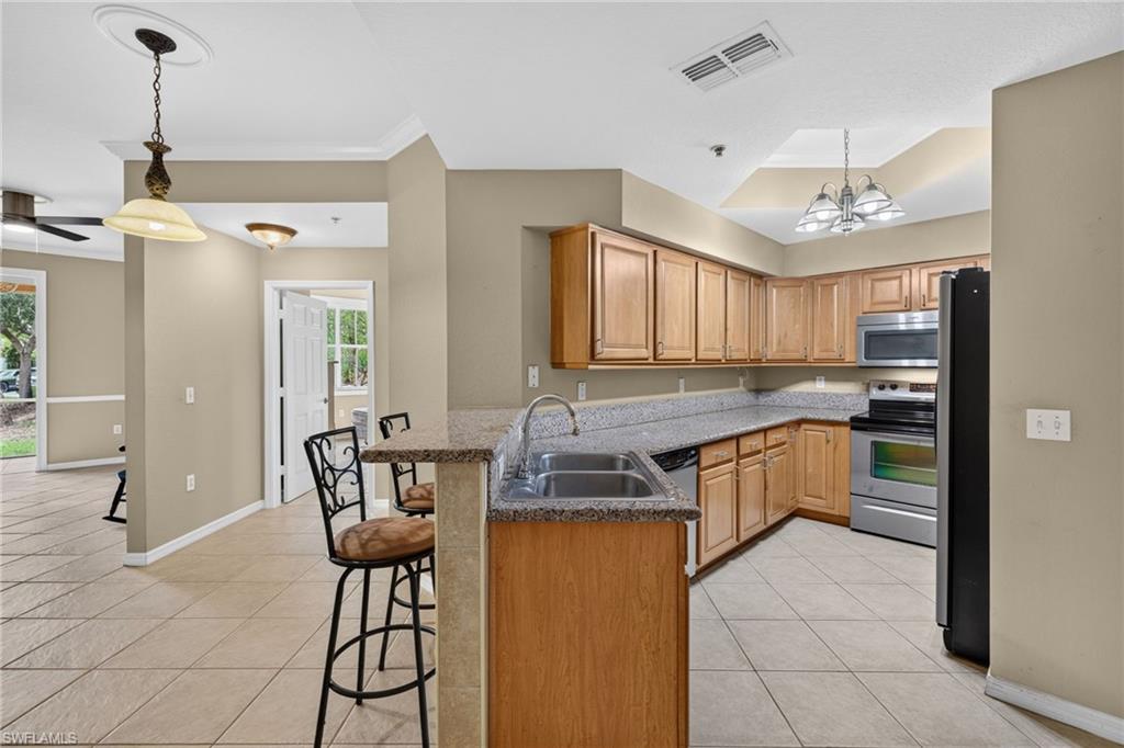 Kitchen featuring wood cabinetry, stainless steel appliances, a double basin sink, and a breakfast bar