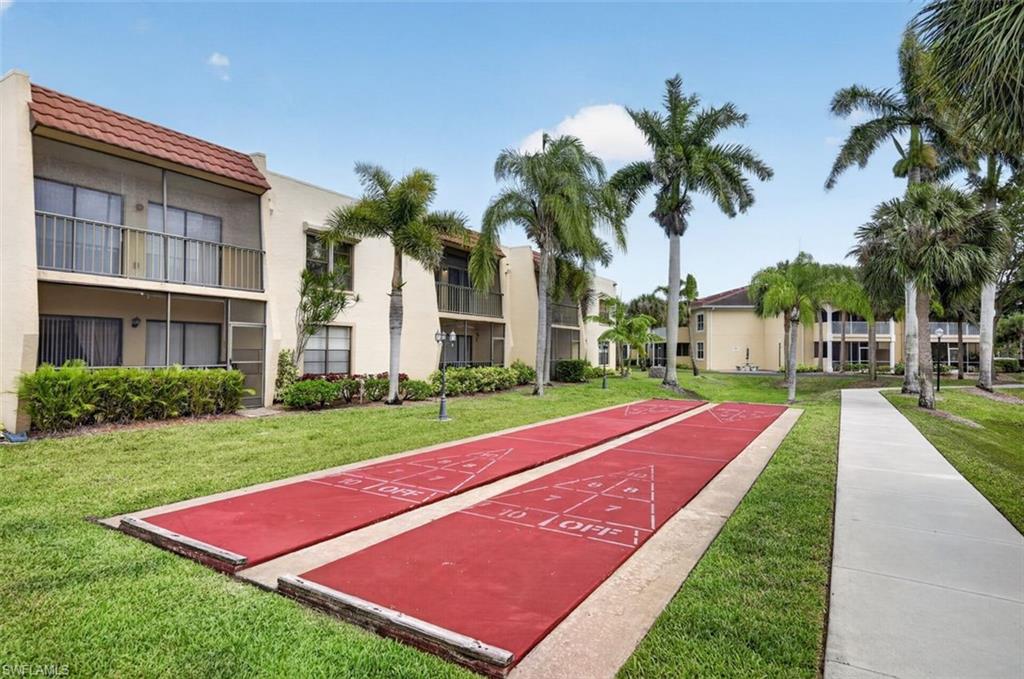 Shuffleboard courts with surrounding manicured lawn, paved walkway, and mature palm trees