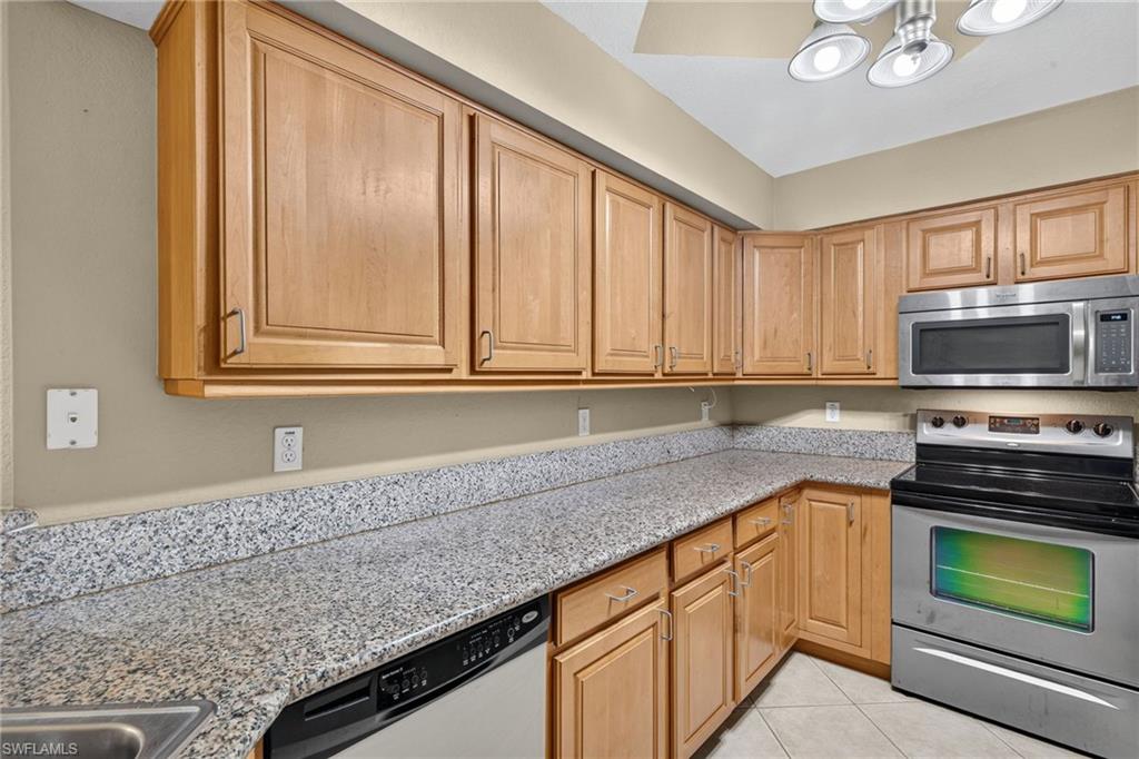 Kitchen featuring light wood cabinetry, stone-finish countertops, stainless steel appliances, and a tile floor