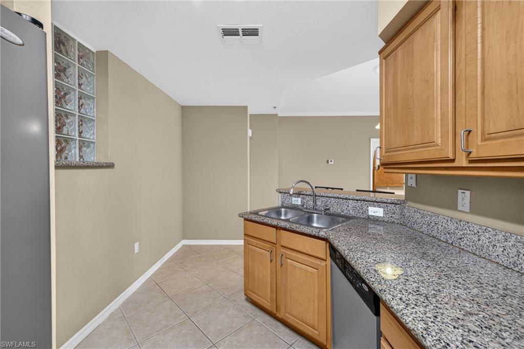 Galley kitchen featuring warm wood cabinetry, speckled stone countertops, stainless steel appliances, tile flooring, and abundant counter space with a functional layout ideal for meal preparation
