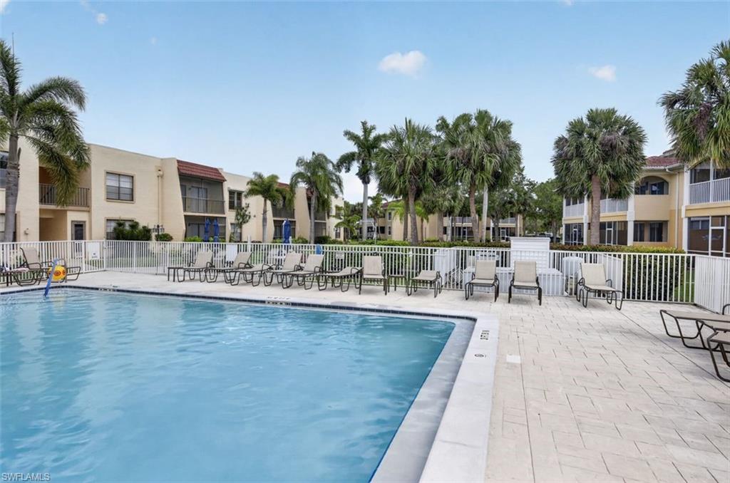 Resort-style pool with a paved deck, surrounded by a white picket fence, and mature palm trees