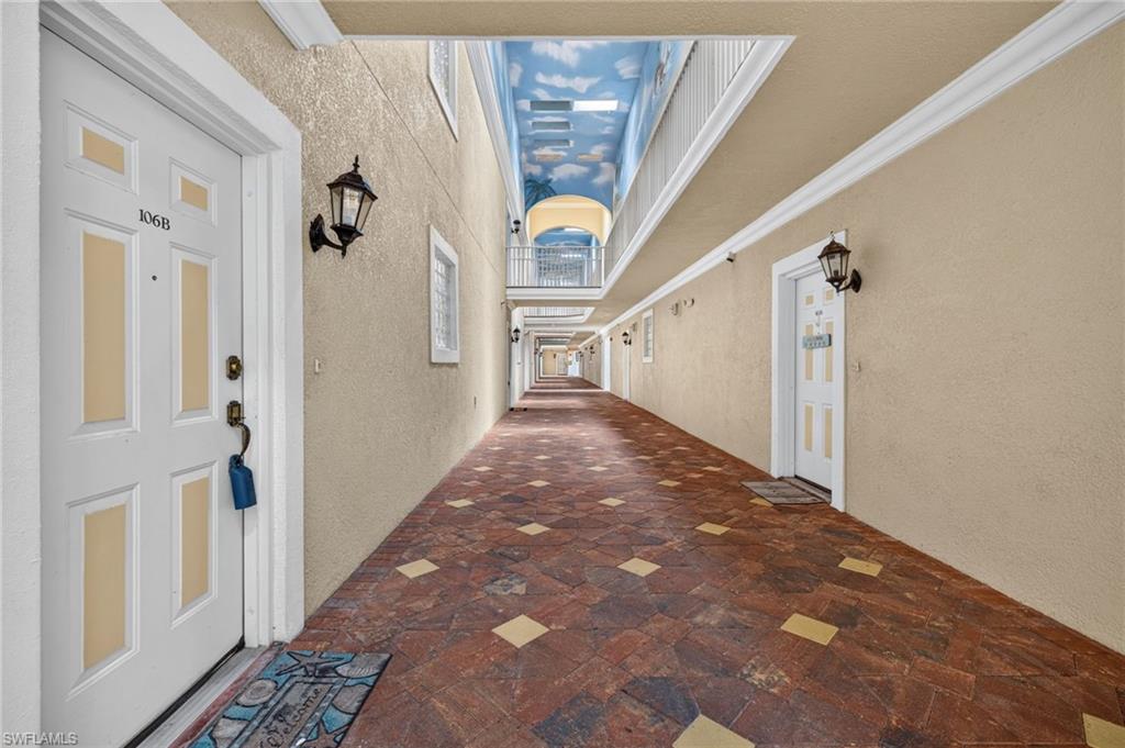 Long hallway with patterned tile flooring, wall-mounted light fixtures, decorative entry doors, and a painted ceiling mural