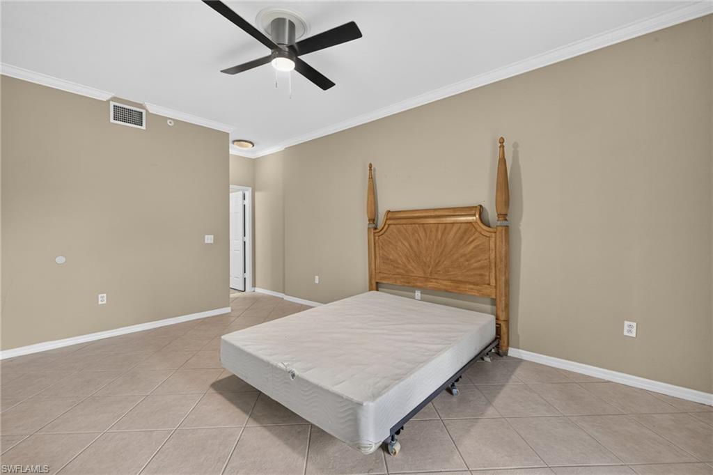 Spacious primary bedroom featuring neutral beige walls, tile flooring, a ceiling fan with integrated lighting, and abundant natural light from multiple windows