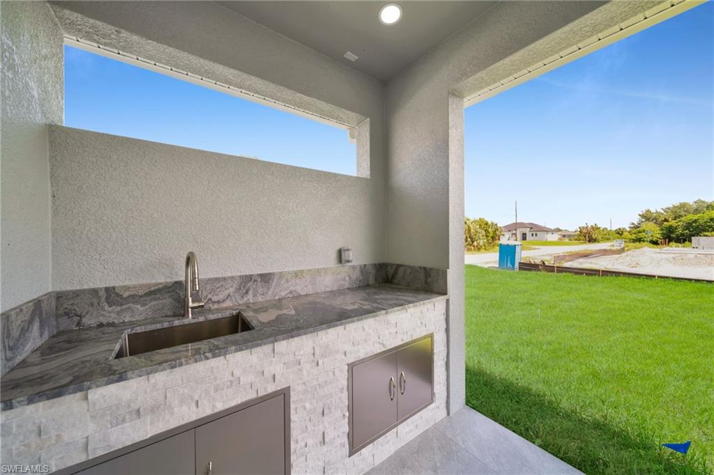 Outdoor kitchen featuring a built-in stainless steel sink, contemporary faucet, stone countertops, and integrated cabinetry with stainless steel doors