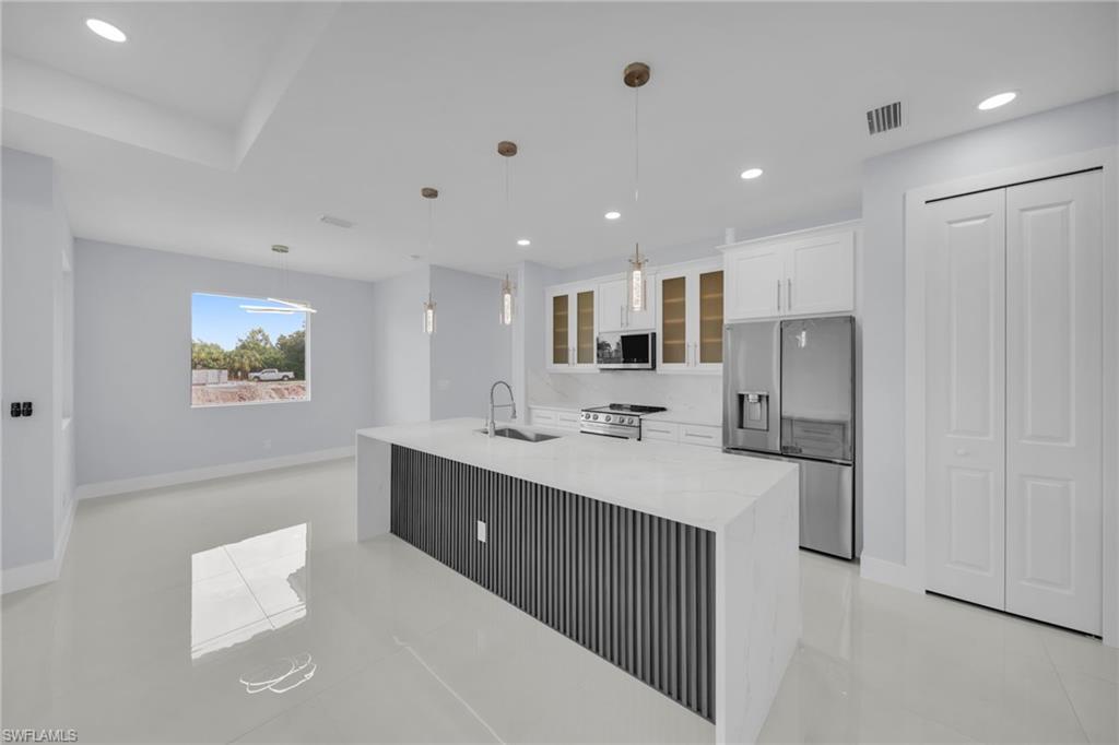 Modern kitchen featuring a waterfall island with a slatted base, stainless steel appliances, white cabinetry, and pendant lighting