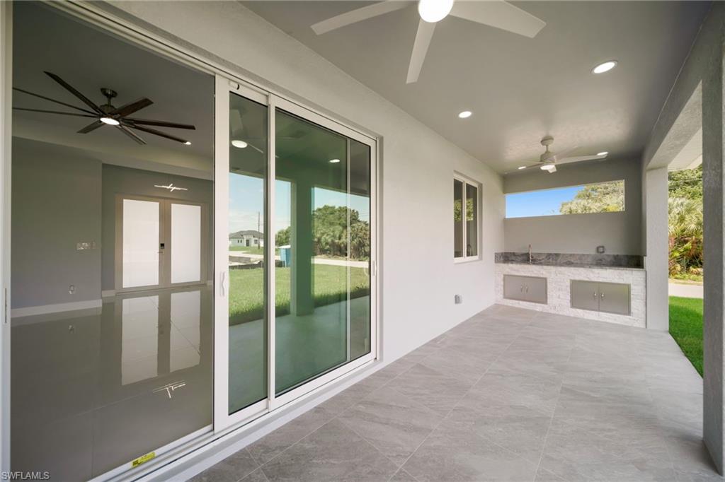 Covered patio featuring large format tile flooring, a built-in outdoor kitchen with stainless steel cabinetry and a sink, recessed lighting, and ceiling fans