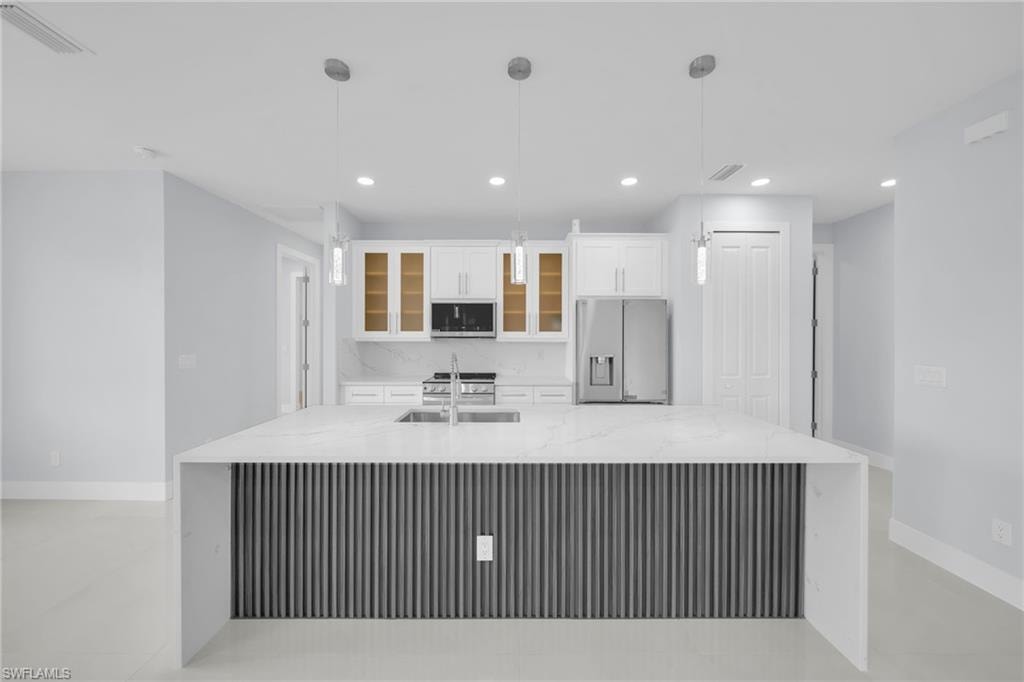 Waterfall-edge island with fluted paneling, quartz countertops, white cabinetry with glass inserts, recessed lighting, and stainless steel appliances