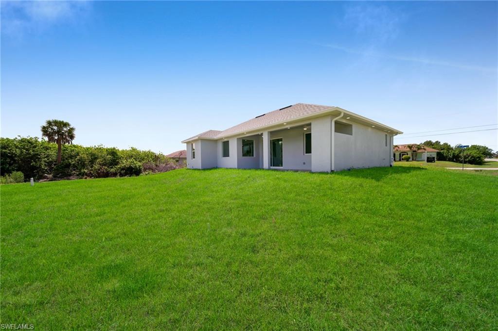 Expansive green lawn with a newly constructed residence featuring a light-colored exterior, covered patio, and large sliding glass doors