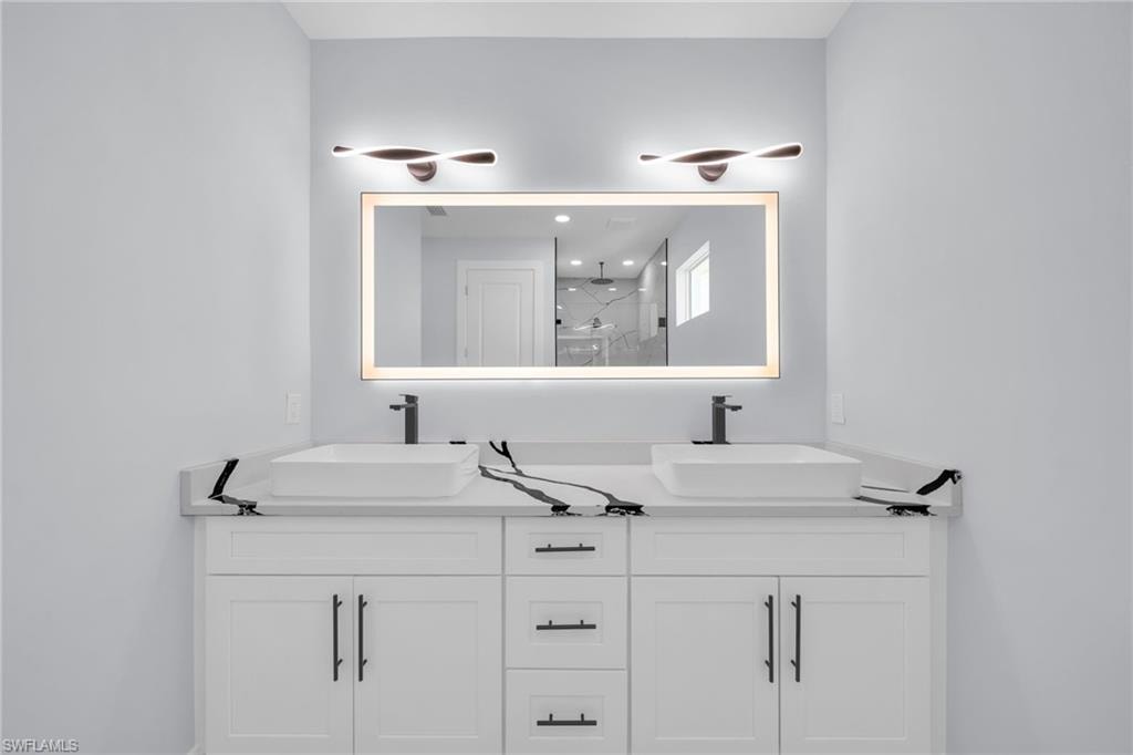 Dual vessel sinks with individual matte black faucets, white shaker cabinetry, a backlit rectangular mirror, and two contemporary vanity light fixtures