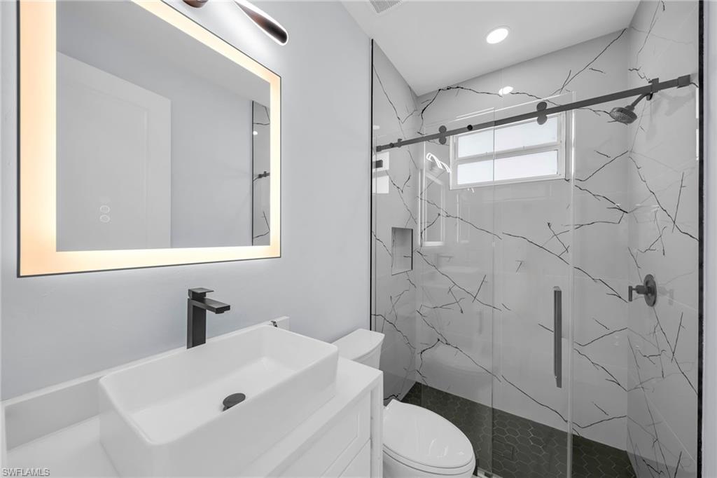Contemporary bathroom featuring a rectangular vessel sink, matte black faucet, illuminated mirror, and a glass-enclosed shower with patterned tile