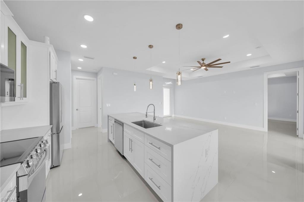 White shaker cabinetry, stainless steel appliances, central kitchen island with integrated sink, recessed lighting, and ceiling fan