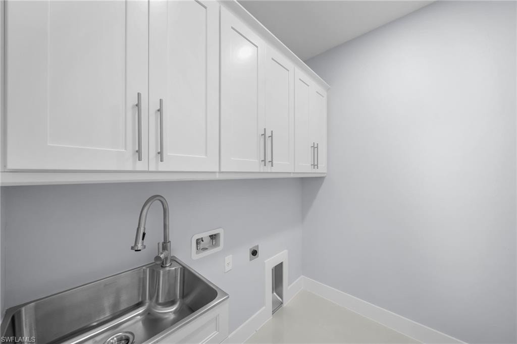 Upper white shaker cabinetry, stainless steel utility sink, gooseneck faucet, light wall color, and light flooring