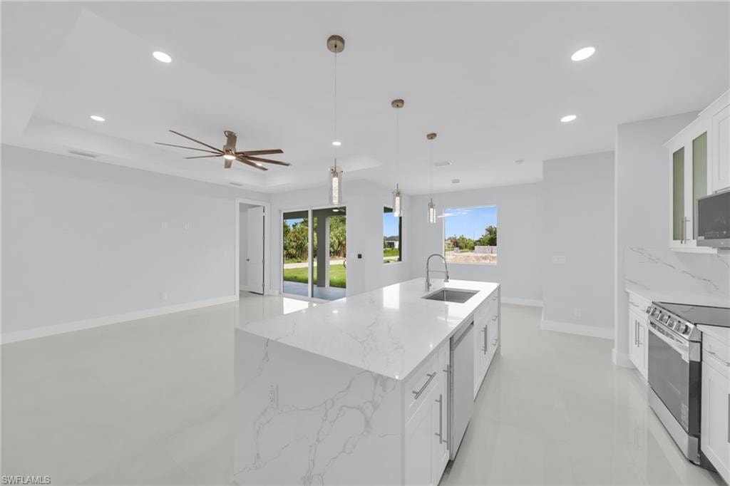 Open-concept living space featuring a spacious kitchen island with integrated sink, stainless steel appliances, recessed lighting, and a modern ceiling fan