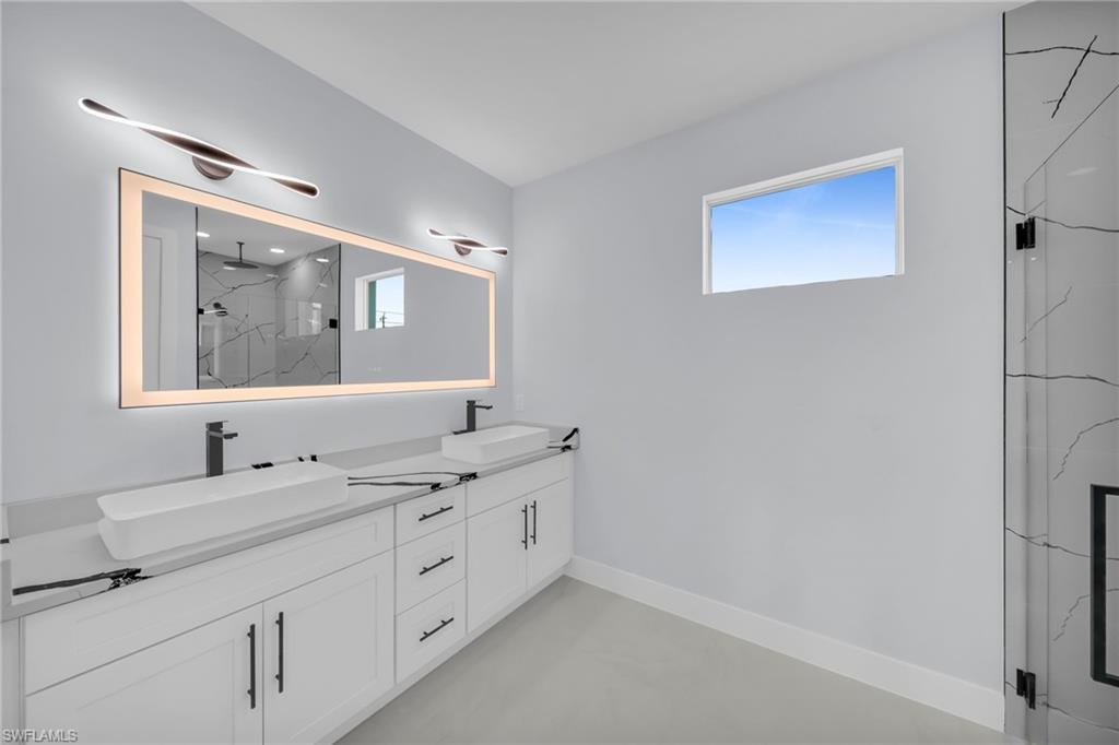 Dual vessel sinks set on a light-toned countertop, complemented by sleek wall-mounted light fixtures and an illuminated mirror