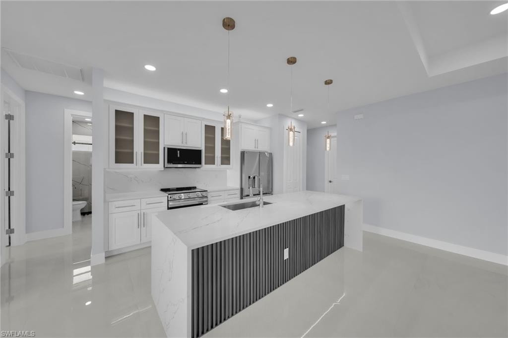 Kitchen featuring a large island with a waterfall countertop, white cabinetry with glass-front uppers, stainless steel appliances, and recessed lighting