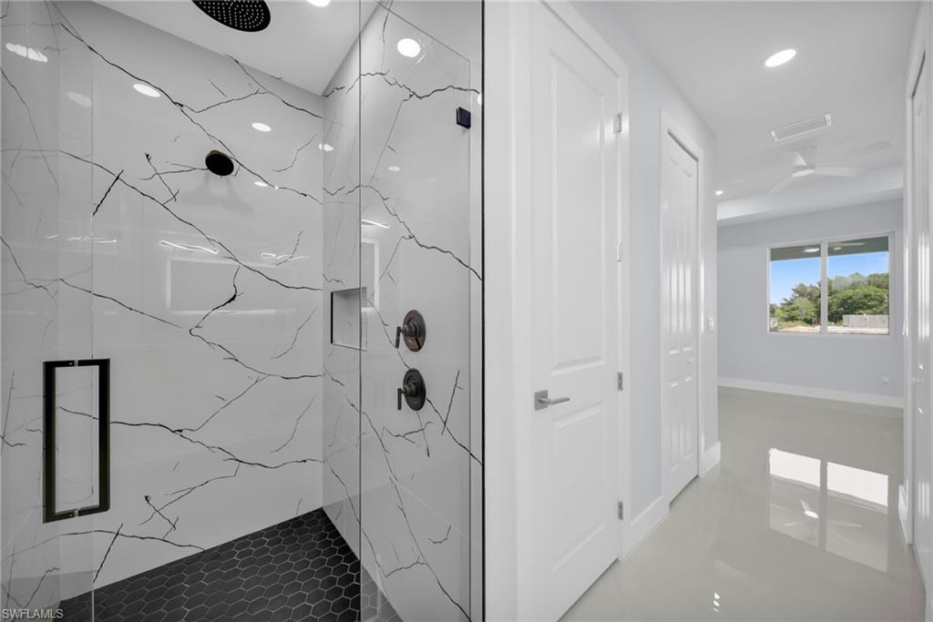 Glass-enclosed shower with black hexagonal tile flooring and large format wall tiles