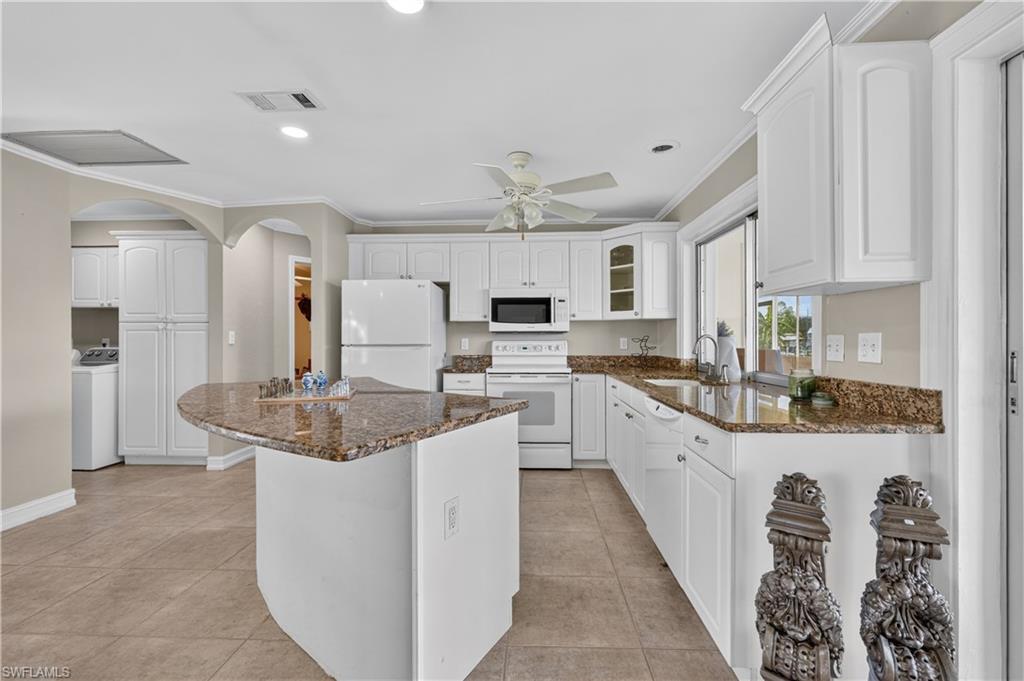 Well-appointed kitchen featuring granite countertops, white cabinetry, tile flooring, a curved island, and a built-in microwave