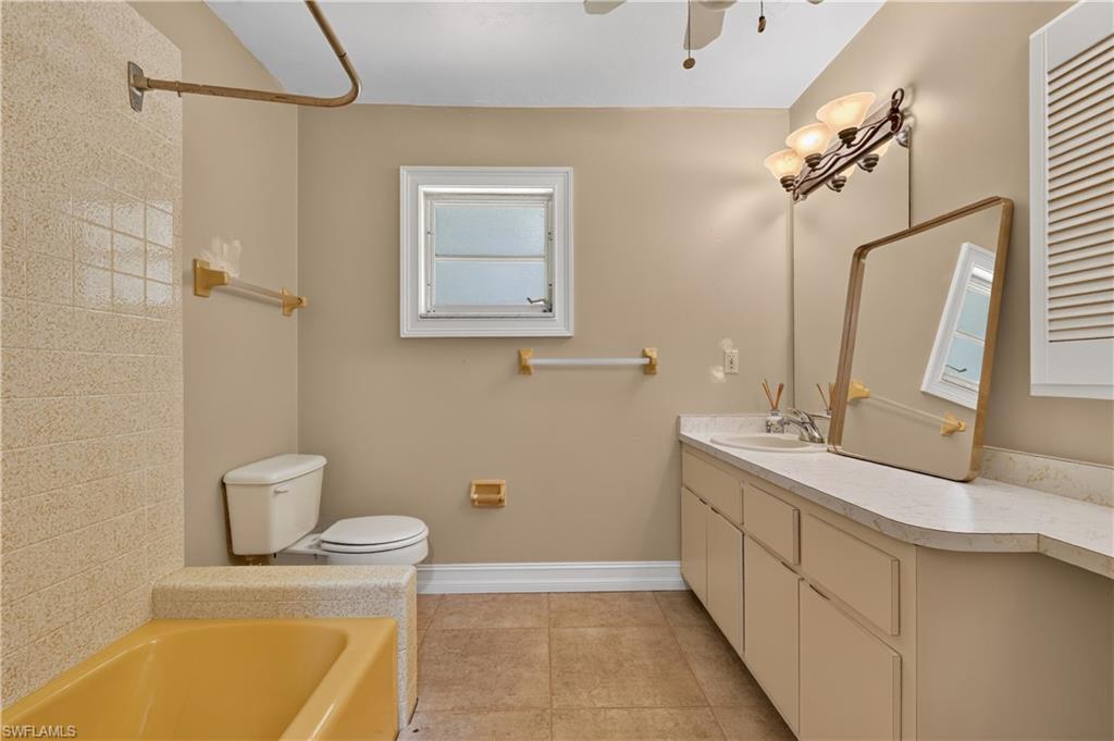 Bathroom featuring a vanity with integrated sink, tile flooring, bathtub with shower surround, and a ceiling fan