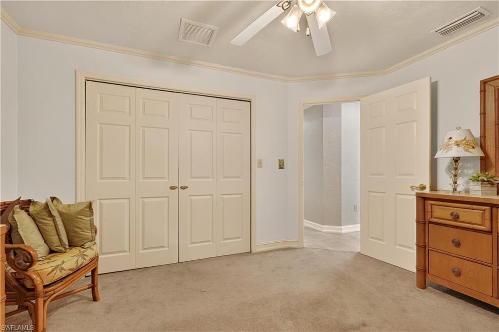 Neutral tone wall paint, crown molding, ceiling fan with light fixture, carpeted flooring, and built-in bi-fold closet doors