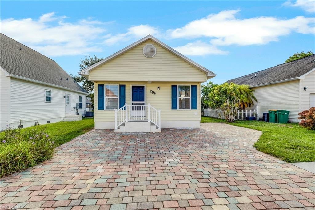 Charming cottage-style residence featuring a cream-colored exterior with blue shutters and trim, complemented by a covered front porch with white railings and columns